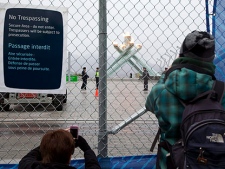 Tourists try to photograph the Olympic Flame through a chain link fence as police stand guard in downtown Vancouver, B.C. Saturday, Feb. 13, 2010. The Vancouver Winter Olympic Games opened on Friday and due to security risks the Olympic caldron is kept behind large fences. (THE CANADIAN PRESS/Jonathan Hayward)