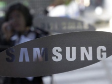 A woman uses her mobile phone near the logo of Samsung Electronics Co. at its headquarters in Seoul, South Korea, Friday, Oct. 29, 2010. (AP Photo/ Lee Jin-man)
