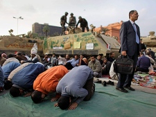 Anti-government protesters pray in front of an army armored vehicle as another dressed in a suit, right, stands to have his picture taken by a friend, at the continuing protest in Tahrir Square in downtown Cairo, Egypt, Monday, Feb. 7, 2011. (AP Photo/Ben Curtis)