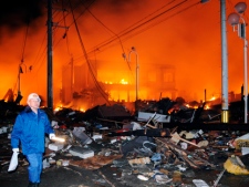 A helmeted man walks past the rubbles and a burning building after a powerful earthquake, the largest in Japan's recorded history, slammed the eastern coasts in Iwaki on Friday, March 11, 2011. (AP Photo/Kyodo News)