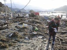 A woman, carrying a child on her back, walks over tsunami-drifted debris and mud on Saturday, March 12, 2011, in Rikuzentakada, Japan. (AP Photo/Kyodo News) 