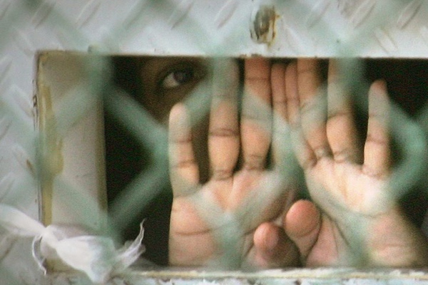A detainee peers through a hole used to allow food and other items into detainee cells at Camp Delta detention center on Guantanamo Bay U.S. Naval Base in Cuba on Dec. 4, 2006. (AP / Brennan Linsley)
