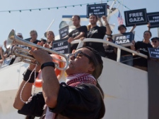An activist plays a trumpet as others hold banners on their boat named "Audacity of Hope" moored in Perama, near Athens, Greece, Thursday, June 30, 2011. Organizers of a pro-Palestinian flotilla that will try to break Israel's sea blockade of the Gaza Strip accused Israel of sabotaging a second ship. (AP Photo/Darko Bandic)