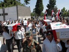 In this photo released by the Syrian official news agency SANA, Syrian policemen carry the coffins of police and army members who were believed killed in recent violence during their funeral procession outside of a hospital in the central city of Homs, Syria, Monday, July 18, 2011. The discovery of three mutilated corpses set off a wave of sectarian bloodshed that killed up to 30 people over the weekend in central Syria, a dangerous escalation in violence stemming from the country's four-month-old uprising, activists said Monday. The Arabic on the coffin right reads: "The martyr policeman Mohammed Massoud." (AP Photo/SANA)