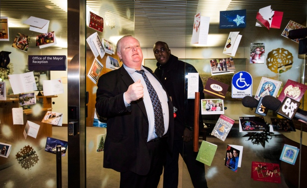 Toronto Mayor Rob Ford, flanked by holiday cards sent to his office, and his driver Jerry Agyemang, right, are seen at city hall on Friday, Dec. 13, 2013. (The Canadian Press/Mark Blinch)