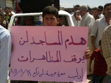 In this citizen journalism image made on a mobile phone and provided by Shaam News Network, an anti-Syrian President Bashar Assad protester holds up an Arabic banner reading :"The destroying of mosques will not stop the demonstrations," during a demonstration against the Syrian regime, at Maarat Harma village, in Edlib province, northen Syria, on Friday Aug. 12, 2011. (AP Photo/Shaam News Network)