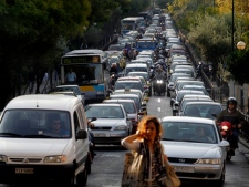 A woman passes a street as motorcyclists make their way through long lines of vehicles in central Athens on Monday, Sept. 26, 2011. The Greek capital faced extensive traffic jams due to a 24-hour Metro, tram and suburban strikes, while buses and trolleys were to stop operating for several hours in the middle of the day. (AP Photo/Petros Giannakouris)