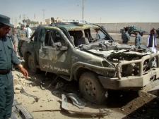An Afghan police officer, left, looks at a police vehicle damaged in a suicide attack in Lashkar Gah, Helmand province, Afghanistan, Tuesday, Sept. 27, 2011. A suicide bomber rammed a car packed with explosives into a police truck outside a bakery in southern Afghanistan on Tuesday, killing a number of civilians, officials said. (AP Photo/Abdul Khaleq)