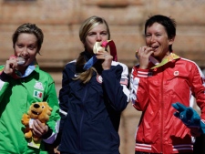 Gold medal winner Heather Irmiger, of the U.S., center, silver medal winner Laura Lorenza Morfin, of Mexico, left, and bronze medal winner Amanda Mae-Ling Sin, of Canada, bite their medals as they stand on the podium for the medal ceremony after the women's cross country mountain cycling event at the Pan American Games in Tapalpa, Mexico, Saturday Oct. 15, 2011. (AP Photo/Jorge Saenz)