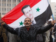 A pro-Syrian regime protester, holds up a Syrian flag bearing a portrait of Syrian President Bashar Assad, in Damascus, Syria, on Wednesday Nov. 16, 2011, during a demonstration against the Arab League meeting being held in Morocco. (AP Photo/Muzaffar Salman)