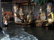 A resident wades through floodwaters as a wave generated by a passing truck hits Buddhist statues at a shop in Bang Khae district of Bangkok, Thailand, Tuesday, Nov. 22, 2011. The situation has improved dramatically in recent days and cleanup has begun in many areas, though some still face weeks more under water. (AP Photo/Sakchai Lalit)