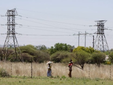 People walk below power pylons at Hartebeespoort, South Africa, Friday Nov. 25, 2011. Eskom is Africa's biggest power utility, accounting for more than 60 percent of all the electricity generated on the continent, according to the World Bank. It also exports across southern Africa. Critics and even supporters say Eskom should have started its move toward renewable sources of energy earlier, and now needs to set its ambitions higher. (AP Photo/Denis Farrell)