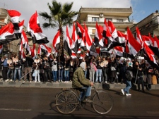 A Syrian man riding his bicycle passes in front of pro-Syrian regime protesters waving their national flags, as they gather outside the Holy Cross Church where a mass prayer was taking place for the people and army soldiers who were killed during the violence around the country, in Damascus, Syria, on Monday Jan. 9, 2012. Thousands of Syrians attended a special prayers held in Damascus for the more than 5,000 people killed since the uprising against President Bashar Assad's regime began in March. The prayers were attended by Christian and Muslim religious leaders.(AP Photo/Muzaffar Salman)
