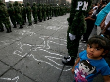 A girl attends a protest organized by the National Regeneration Movement, MORENA, against human rights abuses by military members during the drug war as soldiers stand at attention during a flag-lowering ceremony at the Zocalo central square in Mexico City, Sunday March 4, 2012. Mexico's Defense Secretary Guillermo Galvan conceded on Thursday, Feb. 9, the military has committed errors in the fight against organized crime and drug traffickers such as torture, homicide and drug-trafficking but said those responsible have been punished. The silhouettes, painted on the floor by MORENA members, represent people allegedly killed by soldiers during Mexico's drug war. (AP Photo/Marco Ugarte)
