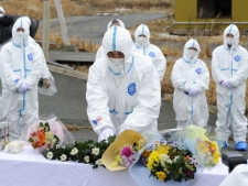 Mourners in protective suits and masks gather for prayers for their beloved ones who was killed in the last year's earthquake and tsunami, inside the contaminated exclusion zone near the crippled Fukushima Dai-ichi nuclear power plant, in Okuma, Fukushima prefecture, Japan Sunday, March 11, 2012. Japan on Sunday was remembering the massive earthquake and tsunami that struck the nation a year ago, killing just over 19,000 people and unleashing the world's worst nuclear crisis in a quarter century. (AP Photo/Kyodo News) 