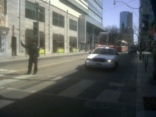 A Toronto police officer directs traffic on Queen Street West at St. Patrick Street on Monday, March 26, 2012. A stretch of Queen Street West was closed after glass reportedly fell from a building. (CP24/Chris Kitching)