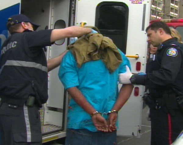 A paramedic attends to the neck wound of a handcuffed man as a police officer hovers nearby on Sherbourne St. on Friday, April 10, 2009.