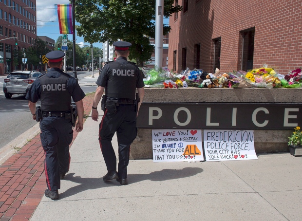 Two officers walk past an array of flowers outside the police station in Fredericton on Friday, Aug. 10, 2018. Two city officers were among four people who died in a shooting in a residential area on the city's north side.THE CANADIAN PRESS/Andrew Vaughan