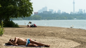A man sleeps on the sandy beach along Lake Ontario in the extreme heat in Toronto on Friday, July 19, 2019. THE CANADIAN PRESS/Nathan Denette