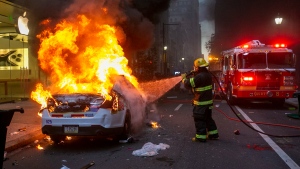 A Philadelphia fire fighter extinguishes a flaming police car in front of the Apple Store on Walnut Street in Philadelphia, Saturday, May 30, 2020, during a protest against the death of George Floyd, a black man who died after a Minneapolis police officer pinned him to the ground with a knee on his neck on May 25. (The Philadelphia Inquirer via AP)