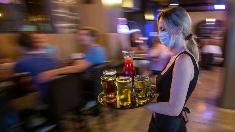Waitress Kirsten Craig wears a mask to curb the spread of COVID-19 while carrying drinks for guests inside the Blu Martini restaurant in Kingston, Ont., on Friday, July 16, 2021. THE CANADIAN PRESS/Lars Hagberg