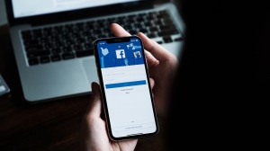 A woman is seen holding an iPhone X to use facebook with new login screen. Facebook is the largest social network and most popular social networking site in the world. (Adobe Stock)