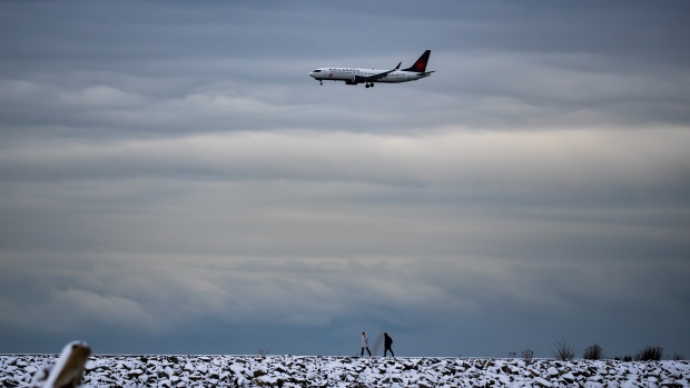 People bundled up for the cold weather walk on the Iona Jetty at Iona Beach Regional Park as an Air Canada plane prepares to land at Vancouver International Airport, in Richmond, B.C., on Sunday, December 26, 2021. THE CANADIAN PRESS/Darryl Dyck