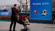 A woman pushing a dog in a pram stops to take a photo of a Beijing Winter Olympics poster on the Olympic Green in Beijing, China, Tuesday, Jan. 18, 2022. China has locked down parts of Beijing's Haidian district following the detection of three cases, just weeks before the capital is to host the Winter Olympic Games. (AP Photo/Ng Han Guan)
