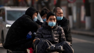 Residents wearing face masks to help curb the spread of the coronavirus ride on a motorized cart on a street in Beijing, Tuesday, Jan. 25, 2022. (AP Photo/Andy Wong)