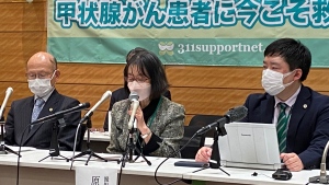 The mother of one of six plaintiffs, center, speaks during a news conference with lawyers after filing their lawsuit at the Tokyo District Court Thursday, Jan. 27, 2022, regarding six people who developed thyroid cancer being connected to the radiation leaked from the Fukushima nuclear power plant accident caused by 2014 the earthquake tsunami. Poster in rear reads "support now for thyroid cancer patients." (AP Photo/Mari Yamaguchi)