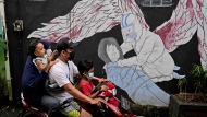 A family wearing masks to help curb the spread of coronavirus outbreak rides on a motorbike past a COVID-19-related mural honoring health workers in Jakarta, Indonesia, Saturday, Jan. 29, 2022. Indonesia is bracing for a third wave of COVID-19 infections as the highly transmissible omicron variant drives a surge in new cases, health authorities and experts said Saturday. (AP Photo/Dita Alangkara)