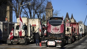 A person walks among trucks as Wellington Street is lined with trucks once again after city officials negotiated to move some trucks towards Parliament and away from downtown residences, on the 18th day of a protest against COVID-19 measures in Ottawa, on Monday, Feb. 14, 2022. THE CANADIAN PRESS/Justin Tang
