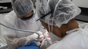 In this Wednesday, May 13, 2020 photo, a dentist, left, and her dental assistant Margot inspect the teeth of a patient  during a dental appointment at a dental office. (AP Photo/Michel Euler) 