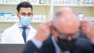 A pharmacist watches Dr Kieran Moore, Ontario's Chief Medical Officer of Health put on his mask at a news conference held in a Toronto pharmacy on Thursday, November 18, 2021. THE CANADIAN PRESS/Chris Young