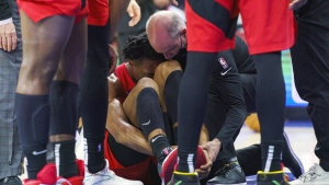 Toronto Raptors' Scottie Barnes, center, gets looked over by the training staff after injuring his left leg during the second half of Game 1 of an NBA basketball first-round playoff series against the Philadelphia 76ers, Saturday, April 16, 2022, in Philadelphia. (AP Photo/Chris Szagola)