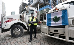 A police officer walks between parked trucks as he distributes a notice to protesters, Wednesday, Feb. 16, 2022, in Ottawa. THE CANADIAN PRESS/Adrian Wyld