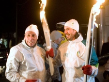 Ivan Reitman, left, pauses after passing the Olympic flame over to his son Jason Reitman as the Vancouver 2010 Olympic torch relay passes through downtown Toronto on Thursday December 17, 2009. (THE CANADIAN PRESS/Chris Young)