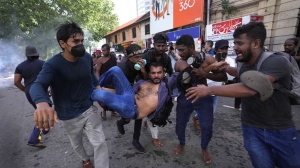 An injured student is carried by colleagues as police fire tear gas and water cannons to disperse protesting members of the Inter University Students Federation during an anti government protest in Colombo, Sri Lanka, Thursday, May 19, 2022. Sri Lankans have been protesting for more than a month demanding the resignation of President Gotabaya Rajapaksa, holding him responsible for the country's worst economic crisis in recent memory. (AP Photo/Eranga Jayawardena)