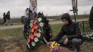 Yura Nechyporenko, 15, places a chocolate at the grave of his father Ruslan Nechyporenko at the cemetery in Bucha, on the outskirts of Kyiv, Ukraine, on Thursday, April 21, 2022. The teen survived an attempted killing by Russian soldiers while his father was killed, and now his family seeks justice. (AP Photo/Petros Giannakouris)
