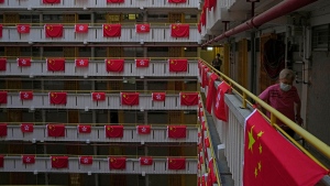 A resident walks besides the Chinese and Hong Kong flags hanging from a residential building to celebrate the 25th anniversary of Hong Kong handover to China, at a public housing estate, in Hong Kong, Saturday, June 25, 2022. As the former British colony marks the 25th anniversary of its return to China, reeling from pandemic curbs that devastated business and a crackdown on its pro-democracy movement, Hong Kong leaders say it is time to transform again and become a tech center that relies more on ties with nearby Chinese factory cities than on global trade. (AP Photo/Kin Cheung)