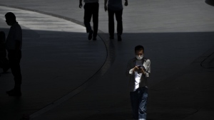 A man wearing a face mask walks through a shopping and office complex in Beijing, Thursday, June 30, 2022. (AP Photo/Mark Schiefelbein)