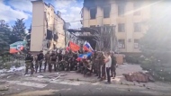 This photo taken from video provided by Ramzan Kadyrov's Official Telegram channel released on Saturday, July 2, 2022 shows Russian troops including soldiers of Chechen regiment waving Russian and Chechen republic national flags as they pose for a photo in front of a destroyed building in Lysychansk, Ukraine. (Ramzan Kadyrov's Official Telegram channel via AP)