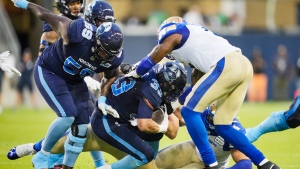 Toronto Argonauts' Andrew Harris, centre, runs the ball with teammate Dejon Allen, left, against Winnipeg Blue Bombers' Willie Jefferson, right, during the first half of CFL football action in Toronto, Monday, July 4, 2022. THE CANADIAN PRESS/Mark Blinch