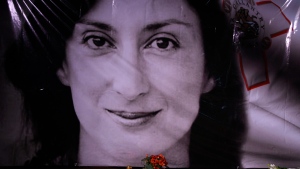 In this Tuesday, Oct. 16, 2018 file photo, flowers and a candle lie in front of a portrait of slain investigative journalist Daphne Caruana Galizia during a vigil outside the law courts in Valletta, Malta. One of three men accused of killing Maltese investigative journalist Daphne Caruana Galizia in a 2017 car bombing changed his plea to guilty during a hearing Tuesday and was immediately sentenced to 15 years in prison. The man, Vince Muscat, together with Alfred and George Degiorgio, had been accused of detonating the bomb that killed Caruana Galizia as she was driving her car Oct. 16, 2017. (AP Photo/Jonathan Borg, File)