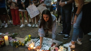 Dozens of mourners gather for a vigil near Central Avenue and St. Johns Avenue in downtown Highland Park, one day after a gunman killed at least seven people and wounded dozens more by firing an AR-15-style rifle from a rooftop onto a crowd attending Highland Park's Fourth of July parade, Tuesday, July 5, 2022 in Highland Park, Ill.. (Ashlee Rezin/Chicago Sun-Times via AP)