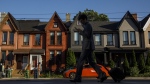 FILE- A person walks by a row of houses in Toronto on Tuesday July 12, 2022. Multigenerations living under one roof is becoming increasingly common, Statistics Canada's latest tranche of census data revealed Wednesday.THE CANADIAN PRESS/Cole Burston