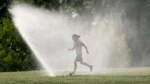 A child runs through a sprinkler as she takes a break from a bike ride near the Ottawa river Tuesday July 7, 2020 in Ottawa. THE CANADIAN PRESS/Adrian Wyld 