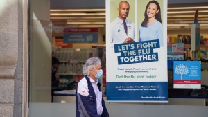 A pedestrian walks by a sign in a store window encouraging people to receive a seasonal flu shot in Toronto on Tuesday, October 19, 2021. THE CANADIAN PRESS/Evan Buhler 