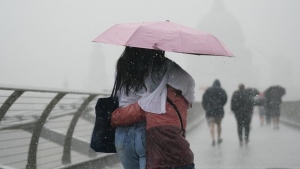People with umbrellas walking in the rain on Millennium Bridge, London, Wednesday Aug. 17, 2022.. After weeks of sweltering weather, which has caused drought and left land parched, the Met Office's yellow thunderstorm warning forecasts torrential rain and thunderstorms that could hit parts England and Wales. (Victoria Jones/PA via AP)