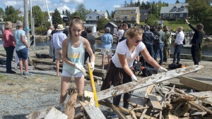 Madelyn Watts, left, and Angelina Taylor clean up debris on the government wharf as Ralph Goodale, minister of Public Safety and Emergency Preparedness and Harjit Sajjan, minister of National Defence, hold a news conference in the background in Herring Cove, N.S. on Tuesday, Sept. 10, 2019. Hurricane Dorian brought wind, rain and heavy seas that knocked out power across the region. THE CANADIAN PRESS/Andrew Vaughan